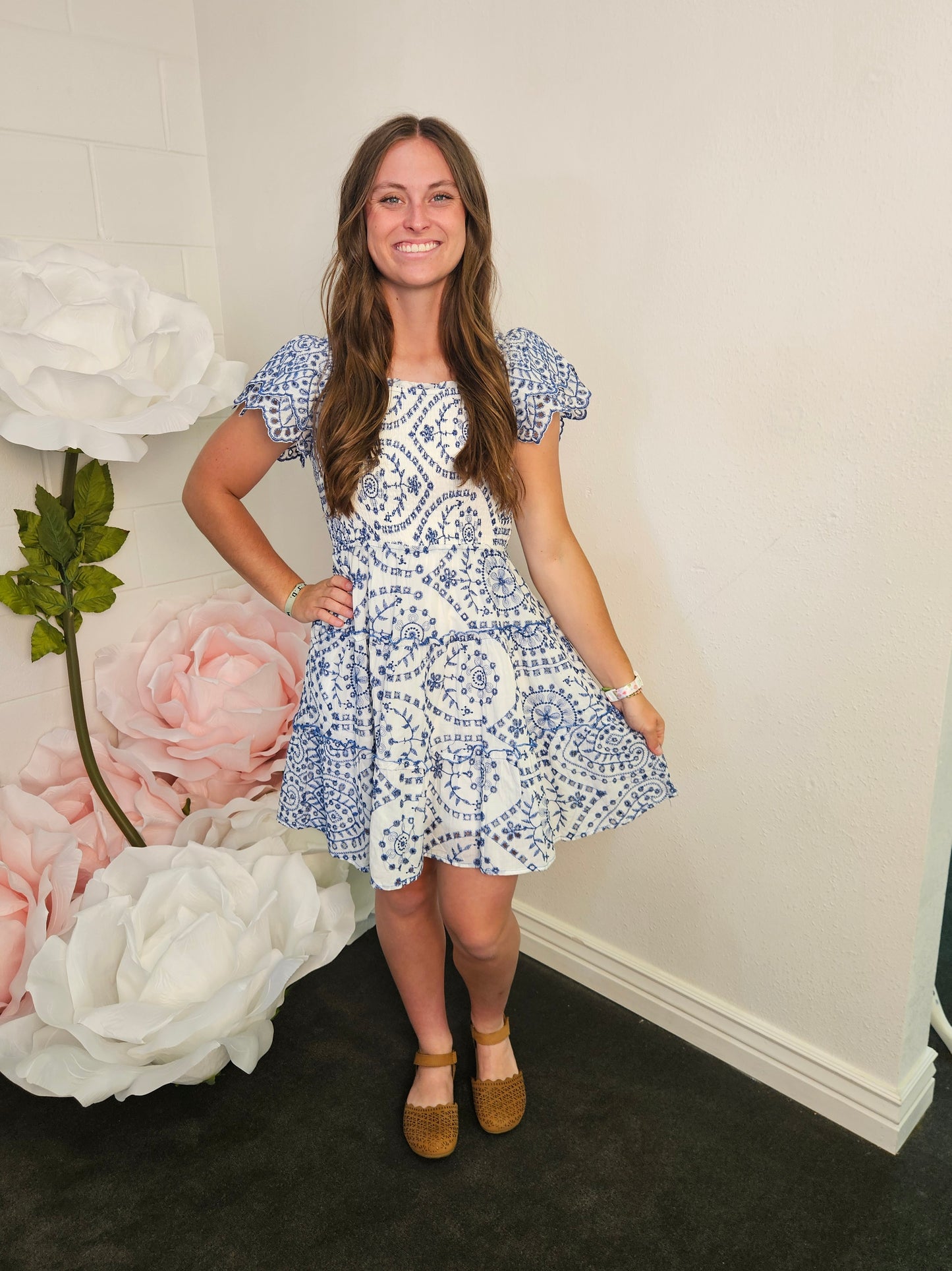 Woman in a blue and white patterned dress standing next to large floral arrangements.