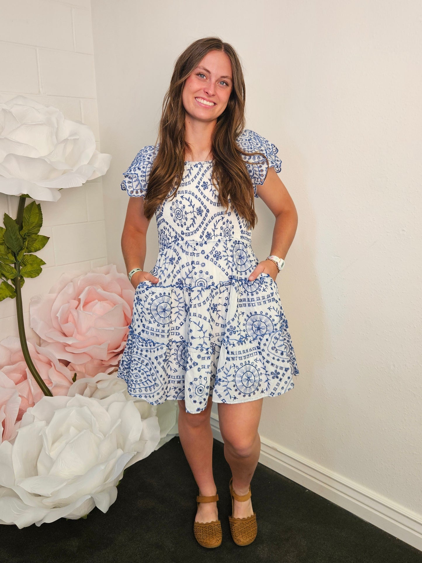 Woman in a blue and white patterned dress standing next to a floral arrangement.